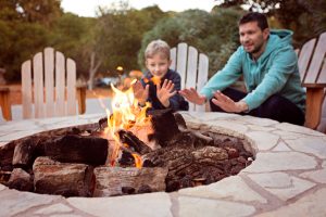 father and son warming their hands around the stone fire pit they built DIY