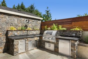 stainless steel outdoor kitchen with stone backsplash and framing on a paver patio